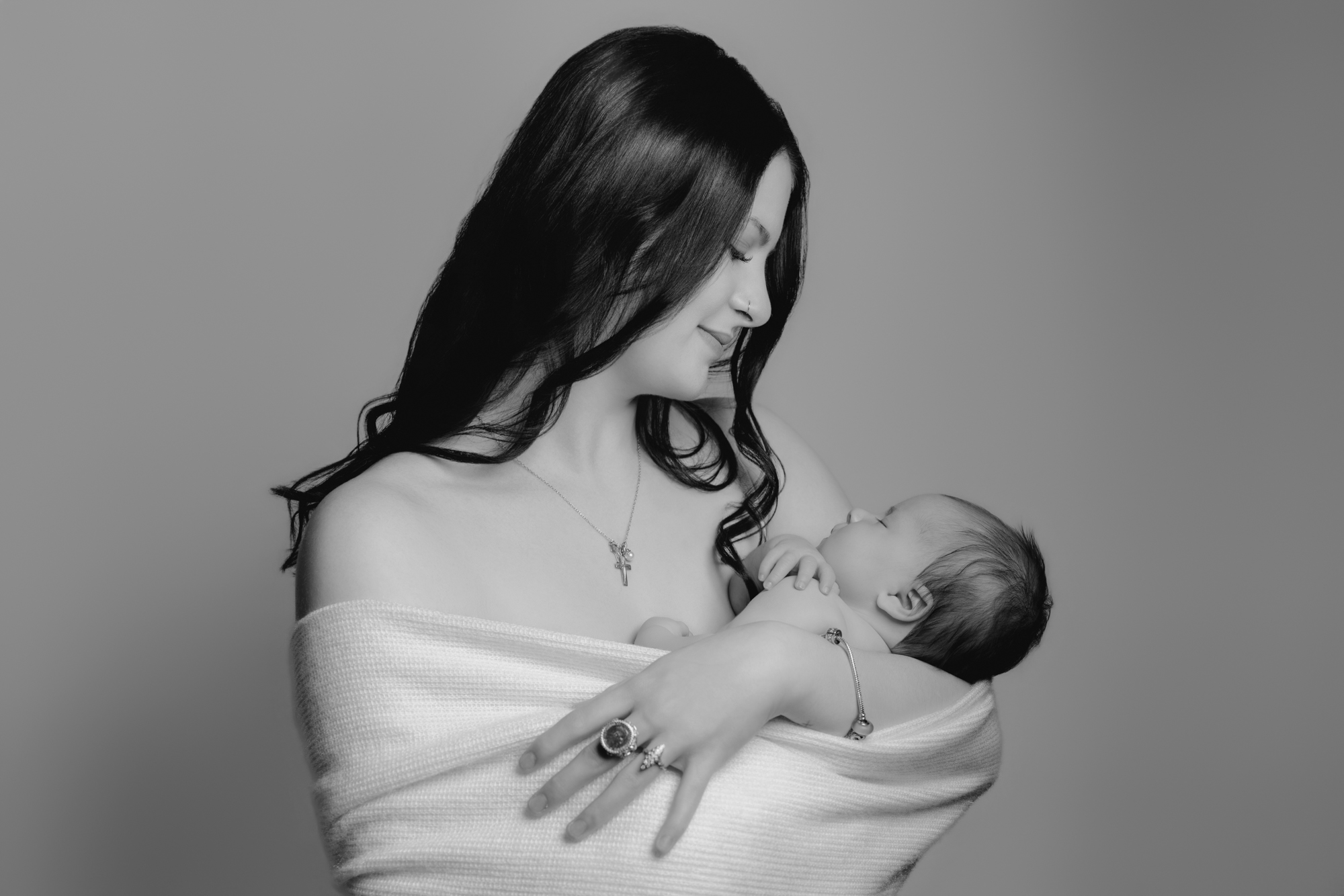 Photo en studio à Maringues. Photo en noir et blanc d'une maman qui porte son bébé dans ses bras, dans une étole de laine. Elle regarde son bébé avec amour et tendresse