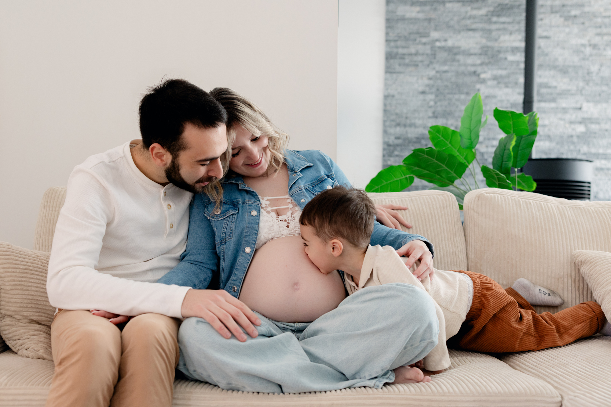 Séance photo grossesse à domicile en Auvergne — famille réunie sur le canapé, futur grand frère embrassant le ventre de maman — Lucile Duvert Photographe Clermont-Ferrand